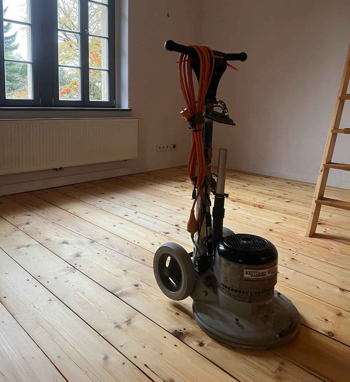 Kaditzianer Bodenschleifmaschine auf einem frisch geschliffenen Holzboden in einem leeren Raum